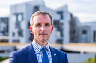 Liam McArthur MSP with the Scottish Parliament behind him